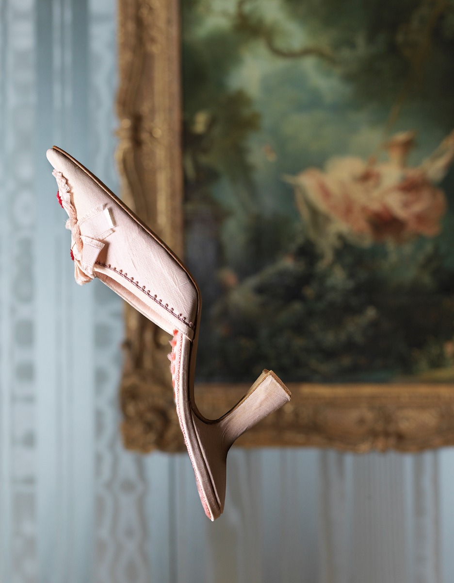 A manolo blahnik shoe suspended in front of a painting