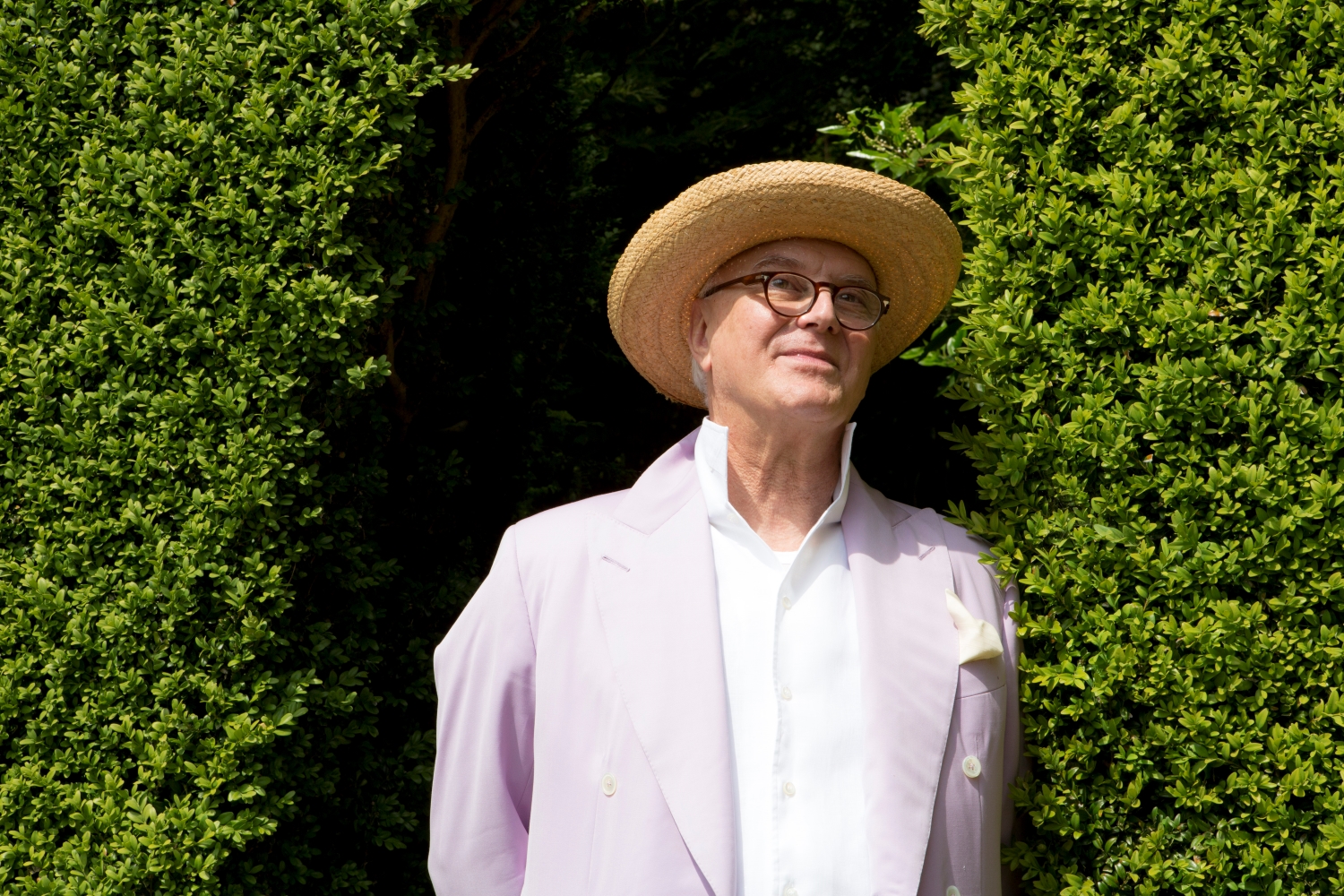 Manolo Blahnik in a garden staring fondly at the nature surrounding him