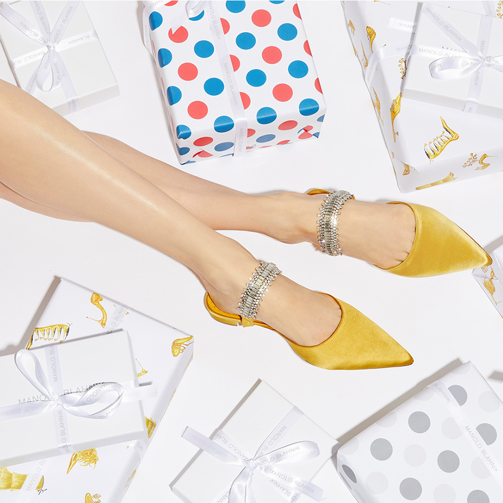 A client trying on the yellow Lutaraflat mules, surrounded by Manolo Blahnik wrapped gifts.