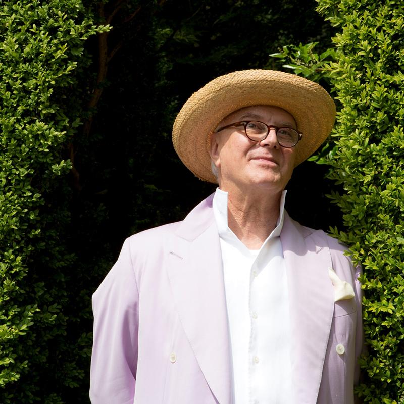 Manolo Blahnik in a garden smiling at the nature surrounding him