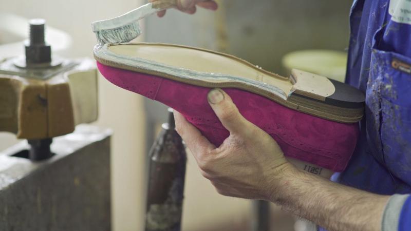 The craftsman applying glue on the shoe's sole.