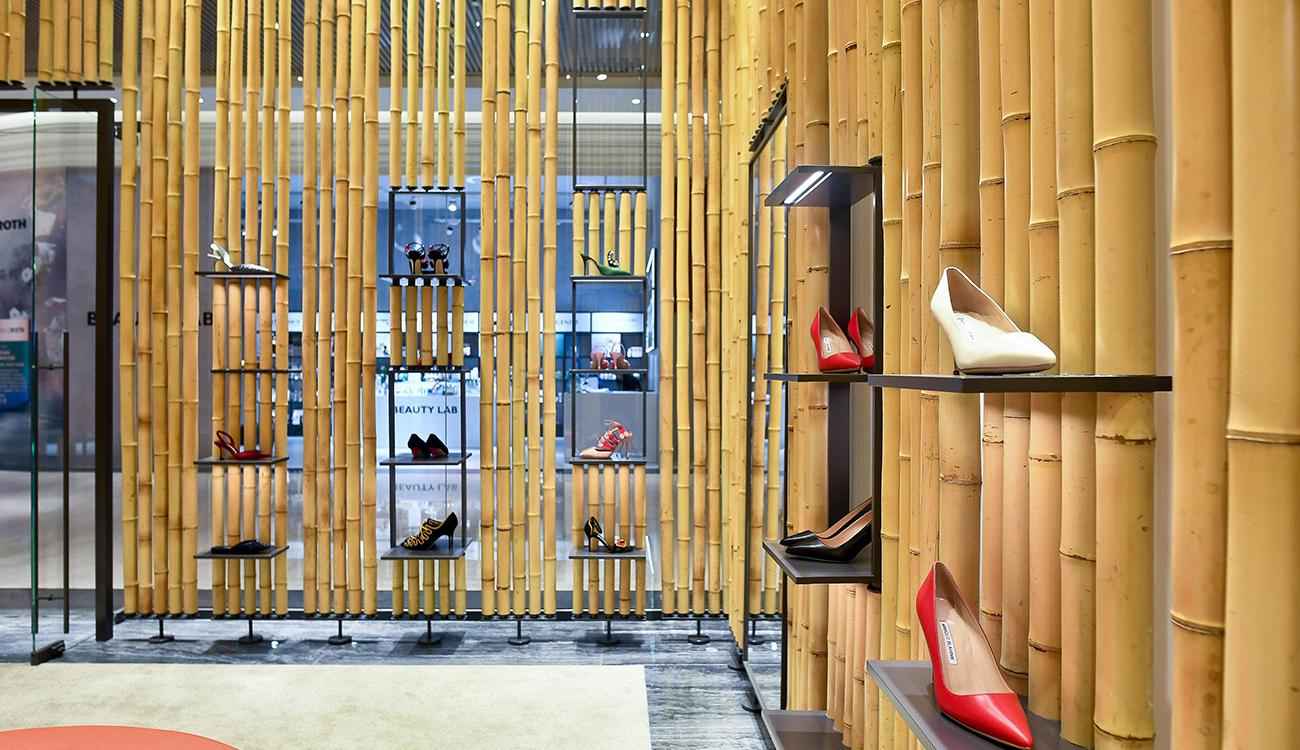 Internal view of the store. The walls are clad with bamboo, with shoes on small shelves. In front there is a round red seat. 