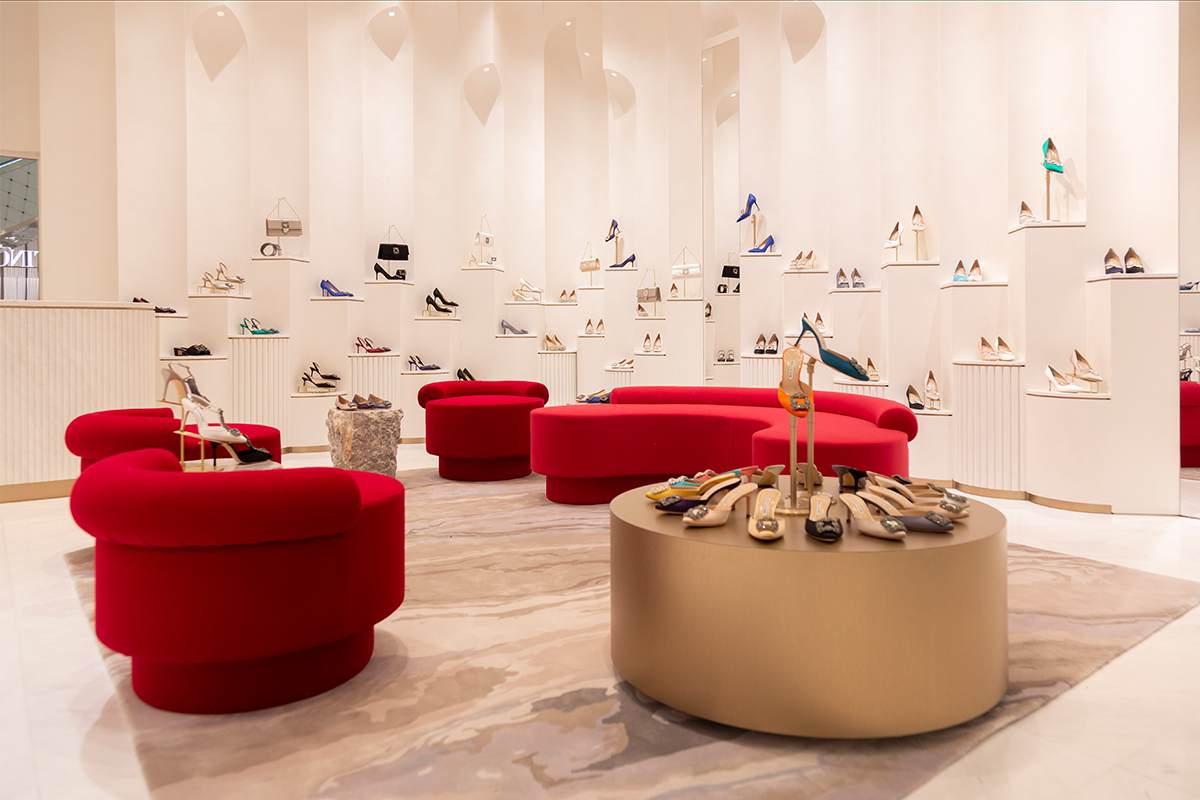 Image of the inside of the Doha Vendome Mall boutique; there are several pillars displaying both classic and seasonal pieces, as well as 4 abstract red sofas in the middle of the store.