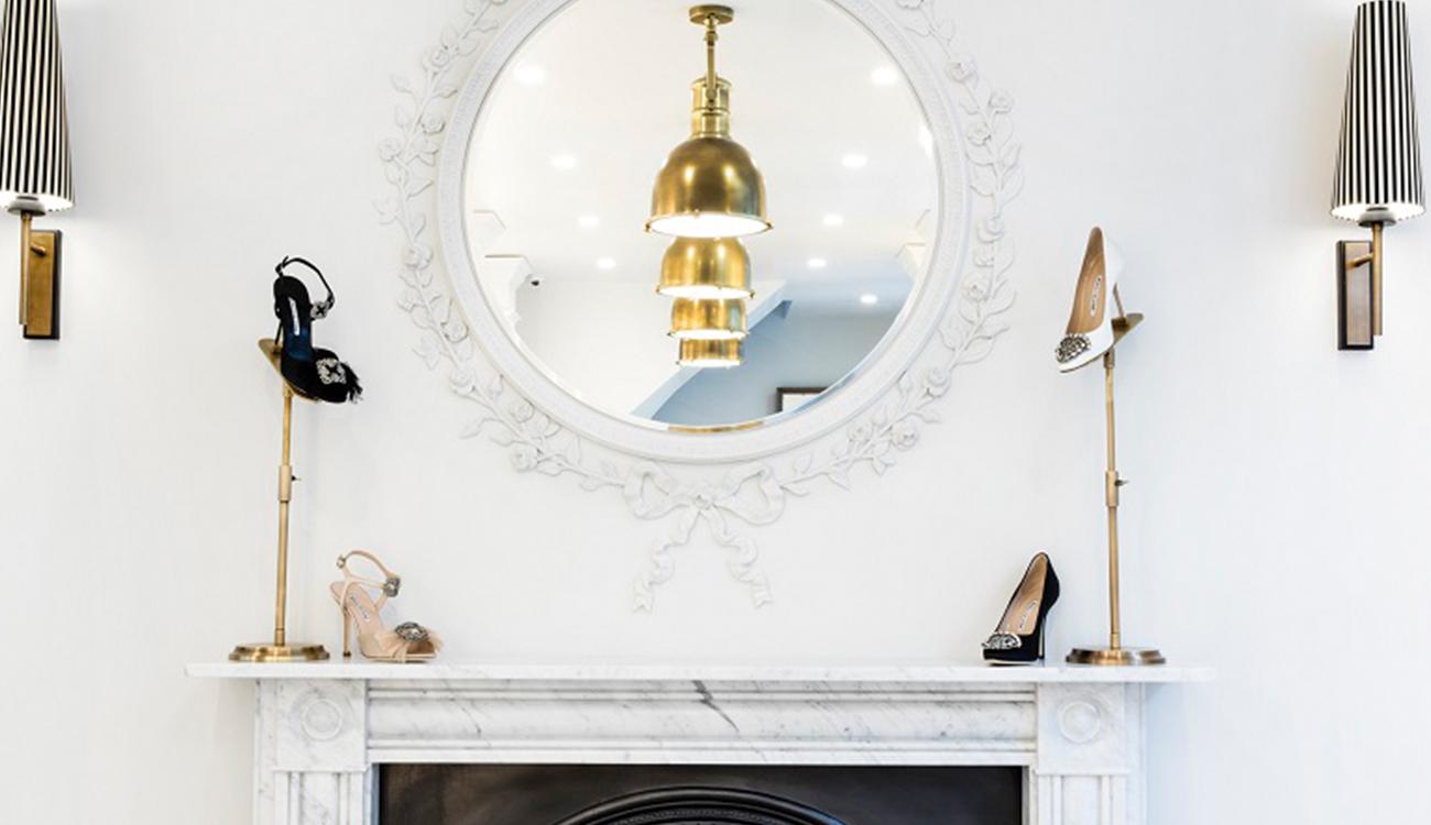 Upstairs in the Burlington Arcade store. A wall with a round mirror, under it, there is a mantel piece with shoes on it. 