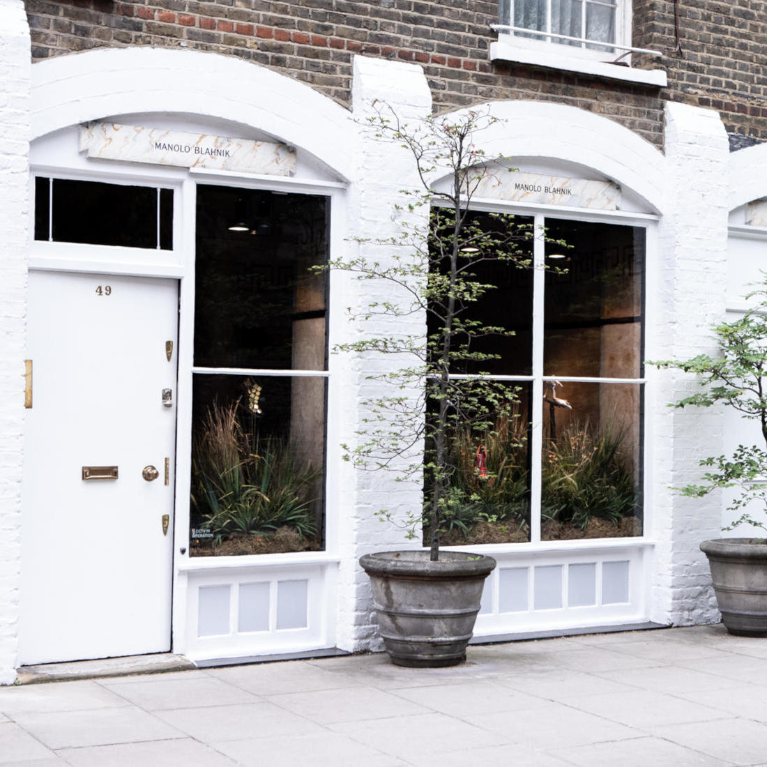 The Old Church Street store. There are large glass windows with arches above them. Two young trees flank the window.