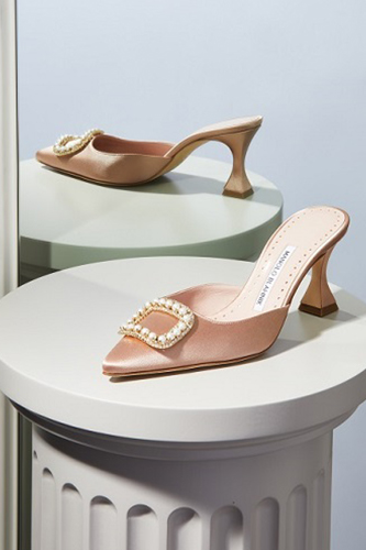A beige satin mule with a pearl buckle displayed on a plinth