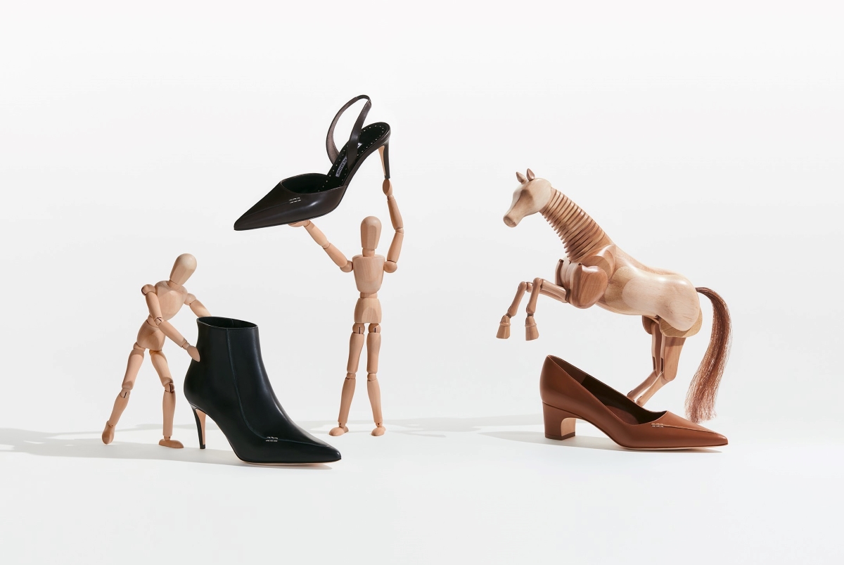 Two wooden dolls and a wooden horse surrounded by a black boot, a dark brown slingback pump and a brown block heel pump.