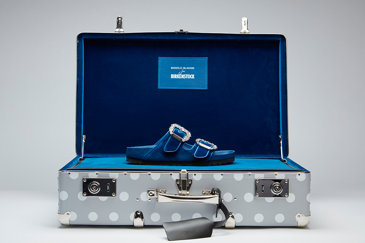 Editorial image of the blue velvet Arizona sandal in a branded grey and white polka dot suitcase.