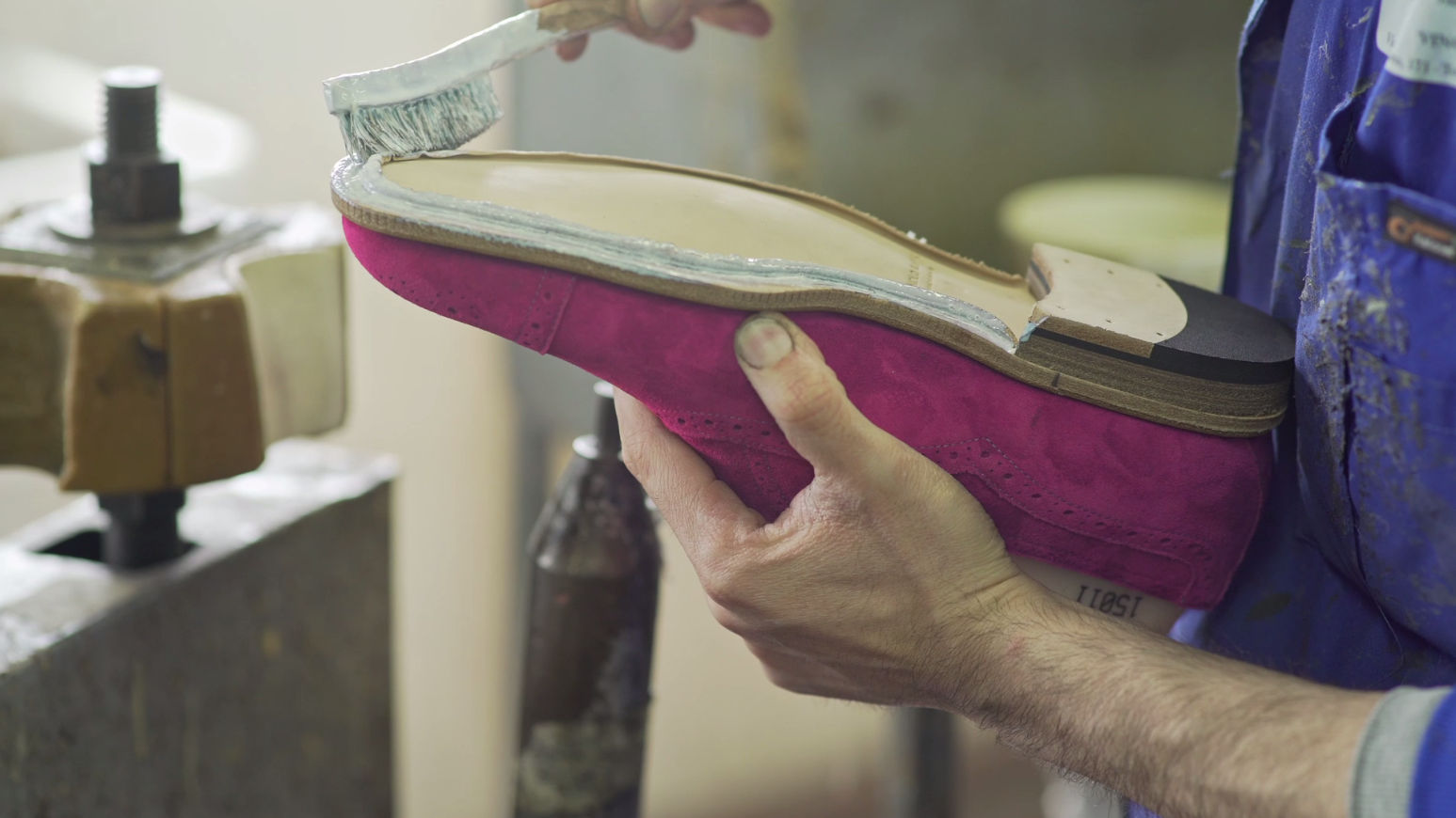 The Witney men’s shoe is upside down in the craftsman’s left hand. In his right hand he is holding a brush covered in glue.