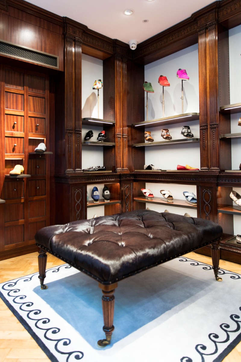 Ground floor of the Men’s store. There is a large brown seat in the middle. On the walls there are shelves with shoes on. 