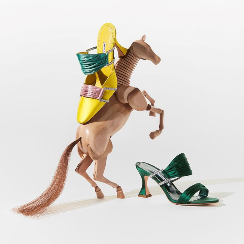 Yellow pump with pink and green gathered straps with embellished detail on wood horse. Green sandal with embellished detail beside this. 