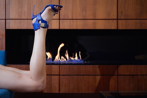 A model kicking up her legs wearing blue sandals in front of a burning fire place