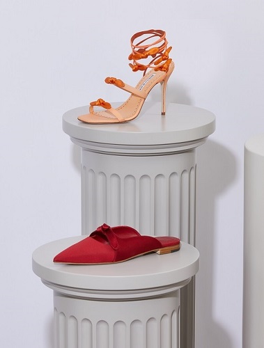 An orange strappy sandal displayed on a plinth