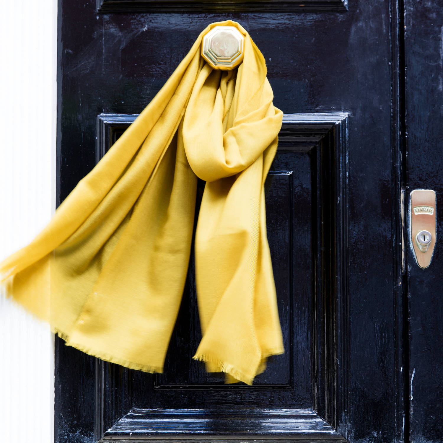 The ‘Iona’ dark yellow superfine cashmere scarf wrapped around an exterior gold door handle.