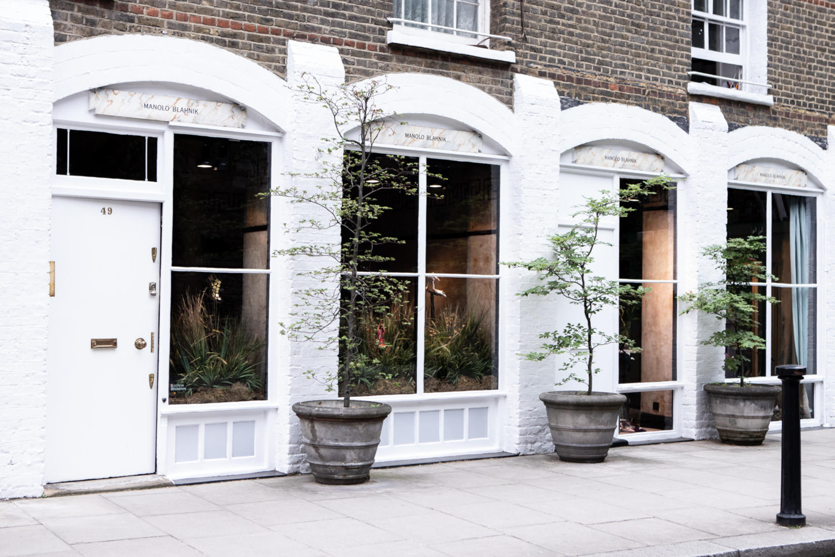 The Old Church Street store. There are large glass windows with arches above them. Two young trees flank the window.
