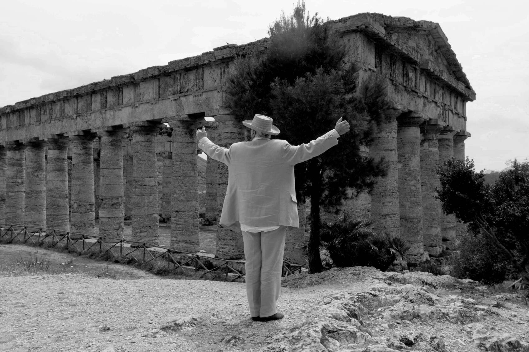 Manolo stood in front of an ancient ruin. He has his back to camera with his arms in the air.