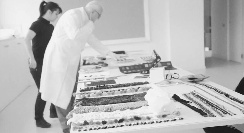 A black and white image of Manolo Blahnik at the factories, he is seen in profile, wearing a white lab coat.